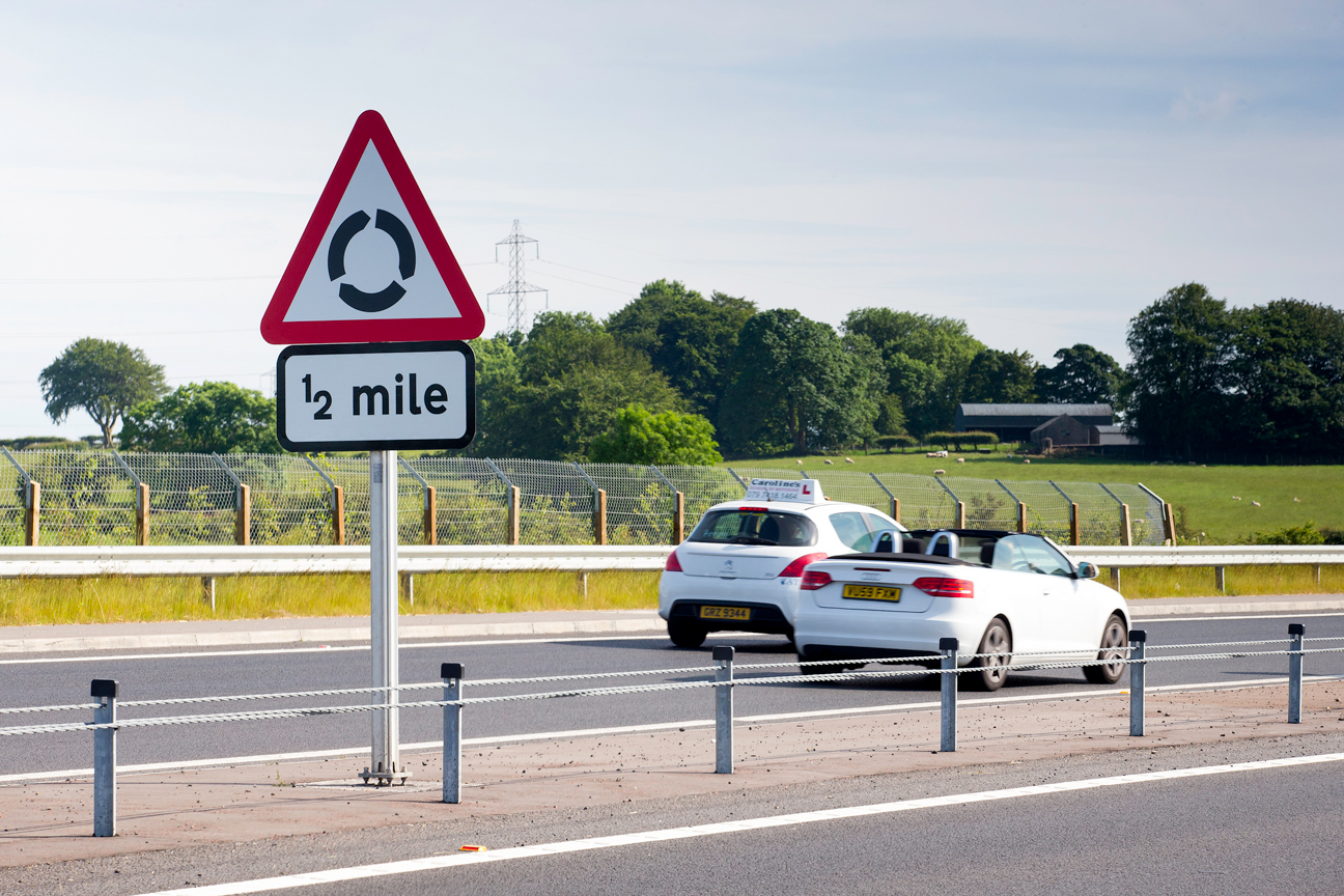 Roundabout road sign with passive sign support and cars driving past